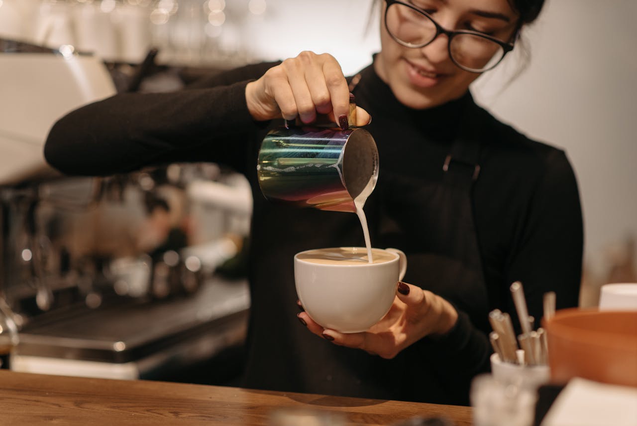 journey Young female barista creating coffee art by pouring milk at a cafe.