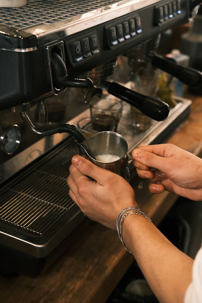 services-03 Barista preparing milk foam at an espresso machine in a cozy café setting.